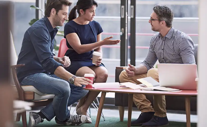 Three colleagues discussing project around table with laptop