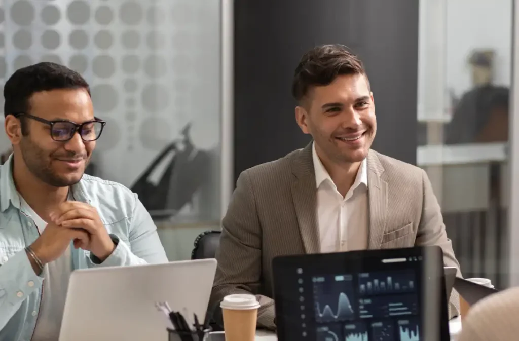 Two businessmen smiling during office meeting with laptops