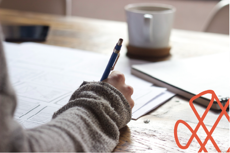 Person writing on documents at desk with coffee