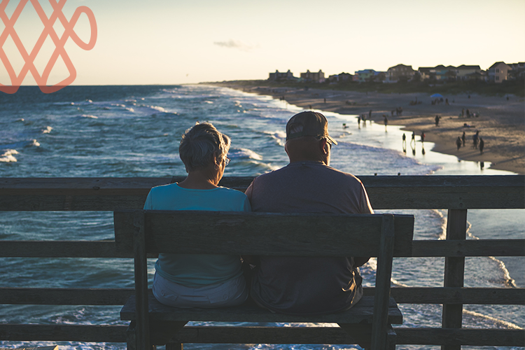 Elderly couple watching ocean sunset from pier bench