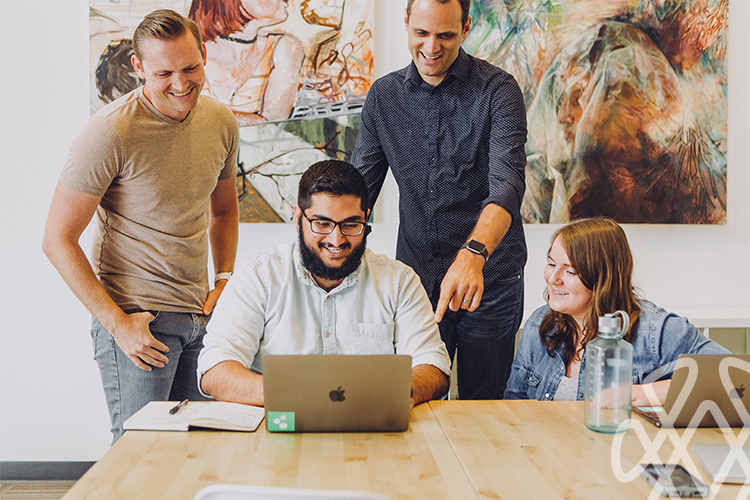 Four coworkers smiling around laptop in office meeting