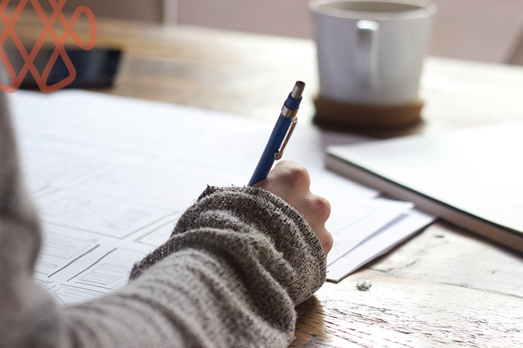 Person writing on paper at desk with coffee