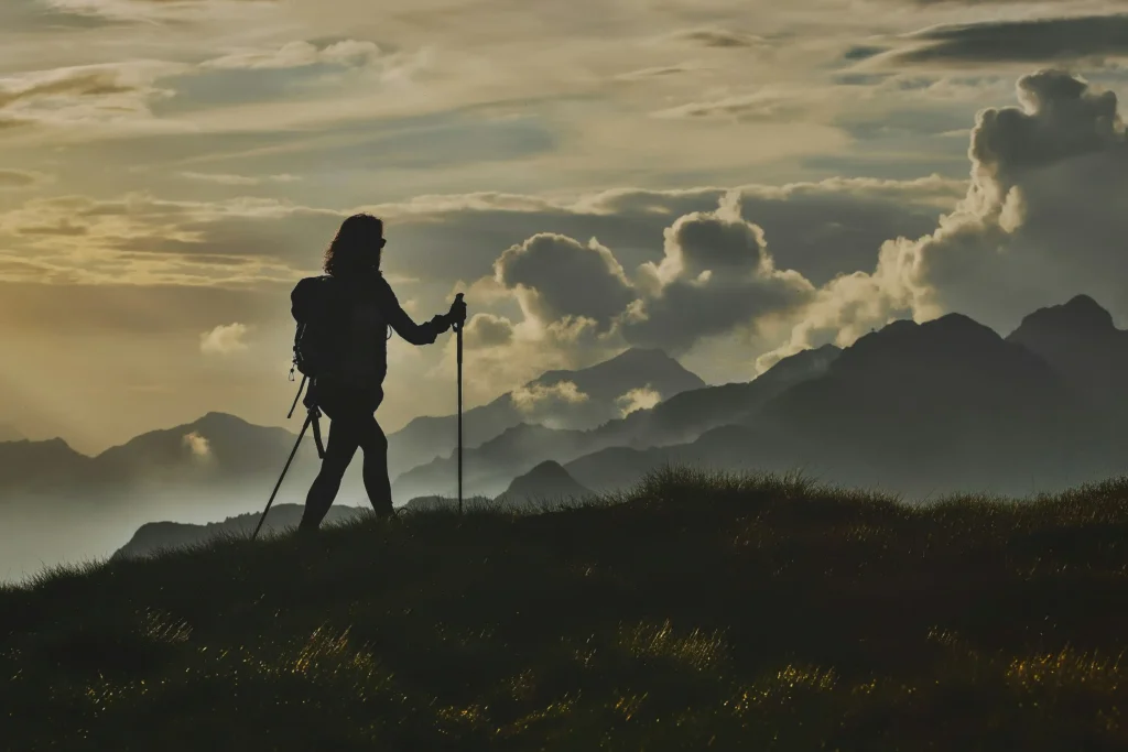 Silhouetted hiker with trekking poles at sunset