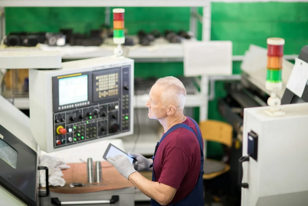 Factory worker operating CNC machine with tablet